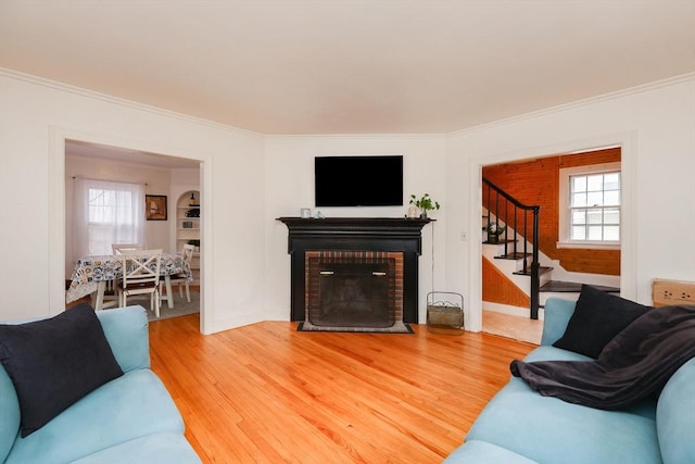 living room with wood-type flooring, a brick fireplace, ornamental molding, and a wealth of natural light