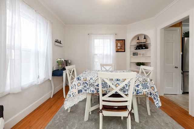 dining room featuring wood-type flooring, crown molding, and built in features