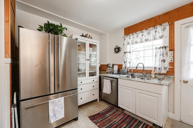 kitchen featuring stainless steel appliances, white cabinets, wood walls, and sink