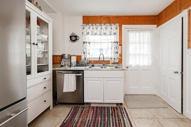 kitchen featuring sink, white cabinets, light stone counters, wood walls, and appliances with stainless steel finishes