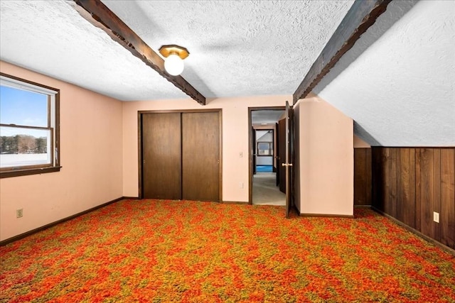 unfurnished bedroom featuring vaulted ceiling with beams, a textured ceiling, and carpet flooring