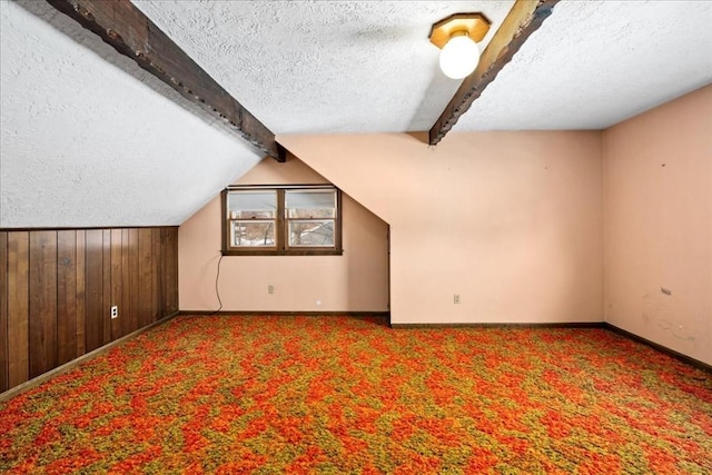 additional living space featuring wooden walls, lofted ceiling with beams, carpet, and a textured ceiling