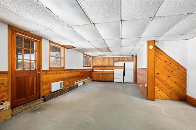 interior space with a paneled ceiling, wooden walls, white fridge, and a baseboard heating unit