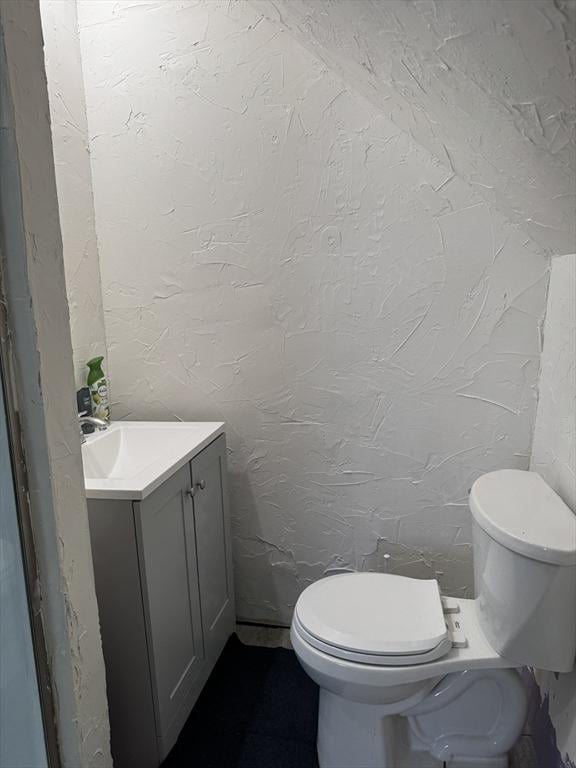 bathroom featuring toilet, vanity, and a textured wall