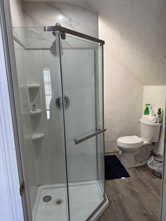 bathroom with toilet, wood finished floors, a shower stall, and a textured wall