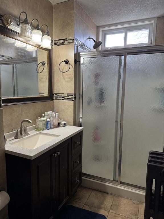 bathroom featuring a textured ceiling, tile walls, a stall shower, and vanity