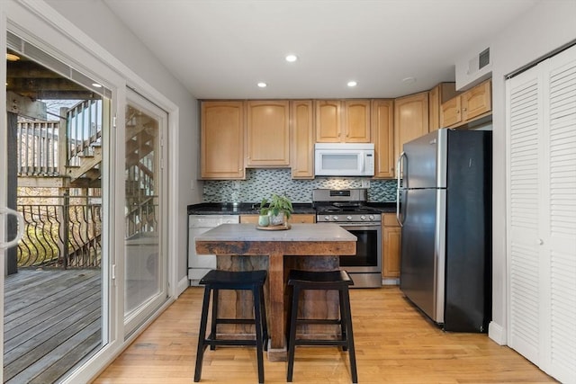 kitchen with a kitchen breakfast bar, tasteful backsplash, stainless steel appliances, light hardwood / wood-style flooring, and a center island