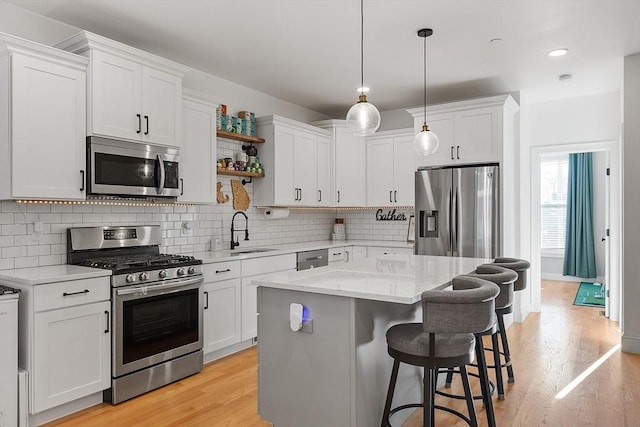 kitchen featuring sink, white cabinetry, a center island, hanging light fixtures, and stainless steel appliances