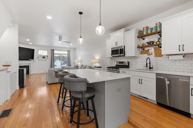 kitchen featuring sink, appliances with stainless steel finishes, white cabinetry, a kitchen breakfast bar, and decorative light fixtures