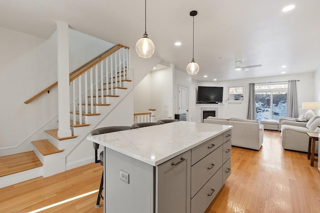 kitchen with gray cabinets, a breakfast bar, hanging light fixtures, a center island, and light hardwood / wood-style floors