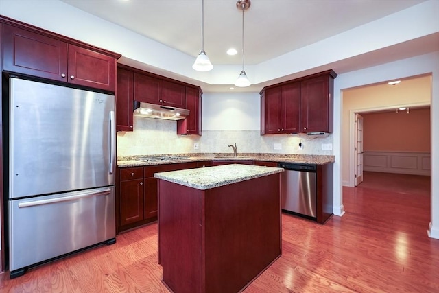 kitchen with a center island, sink, hanging light fixtures, appliances with stainless steel finishes, and light stone counters