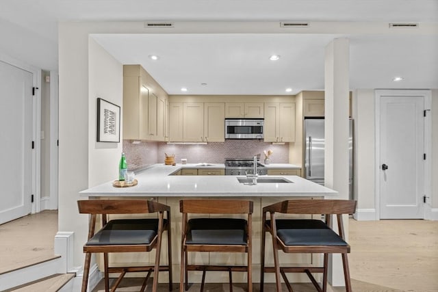 407 Shawmut Ave Unit 1, Boston, MA 02118 - kitchen featuring stainless steel microwave, a peninsula, light wood-style floors, tasteful backsplash, and a kitchen bar