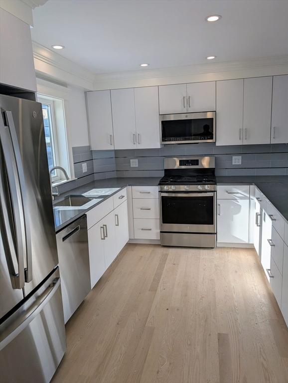 kitchen featuring light wood-style flooring, a sink, stainless steel appliances, dark countertops, and backsplash