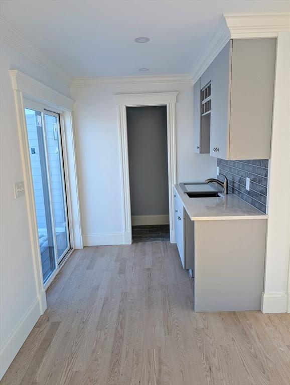 kitchen featuring a sink, light wood finished floors, crown molding, and light countertops