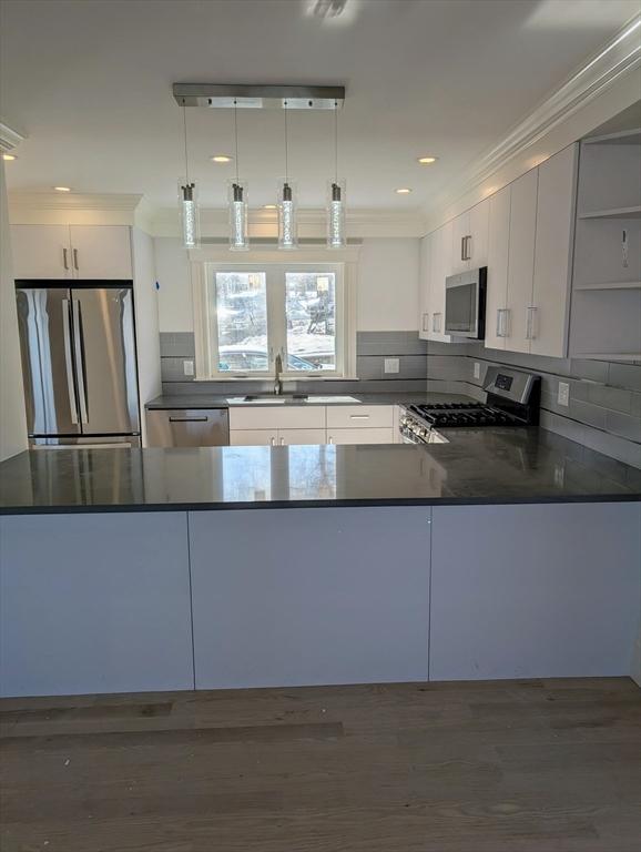 kitchen with dark countertops, appliances with stainless steel finishes, a peninsula, and ornamental molding