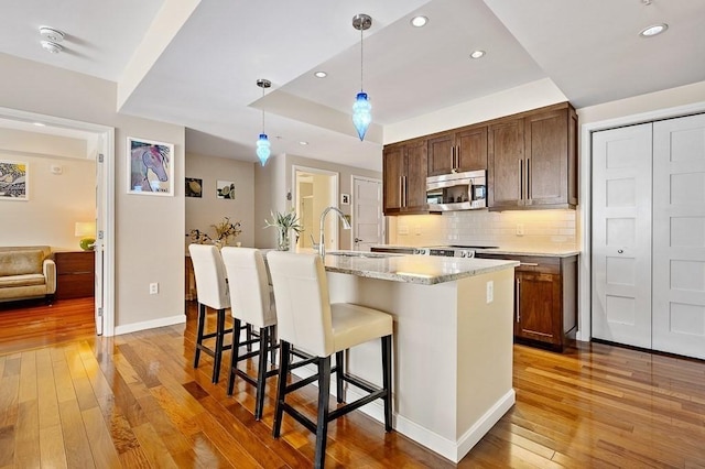 kitchen featuring a kitchen island with sink, hanging light fixtures, light hardwood / wood-style flooring, and sink