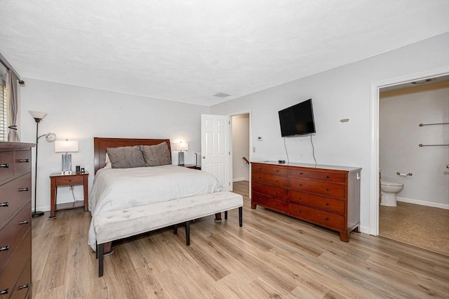 bedroom with ensuite bath, light wood-style flooring, and baseboards