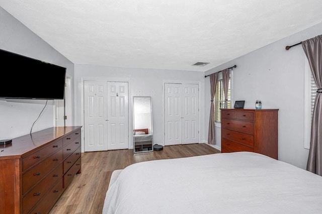 bedroom with multiple closets, light wood-type flooring, and visible vents