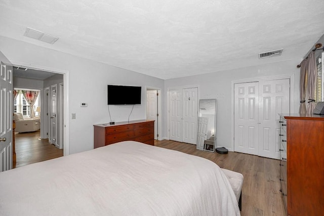 bedroom with multiple closets, visible vents, and wood finished floors