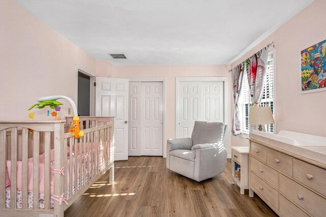 bedroom featuring a crib, visible vents, multiple closets, and wood finished floors