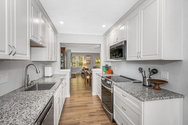 kitchen with stainless steel appliances, a sink, white cabinets, light stone countertops, and light wood finished floors