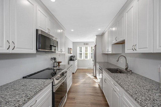 kitchen featuring light stone counters, appliances with stainless steel finishes, white cabinets, and a sink