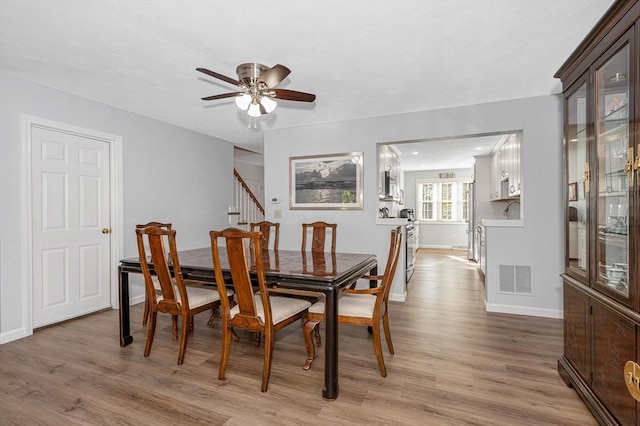 dining area with light wood finished floors, baseboards, stairway, and visible vents