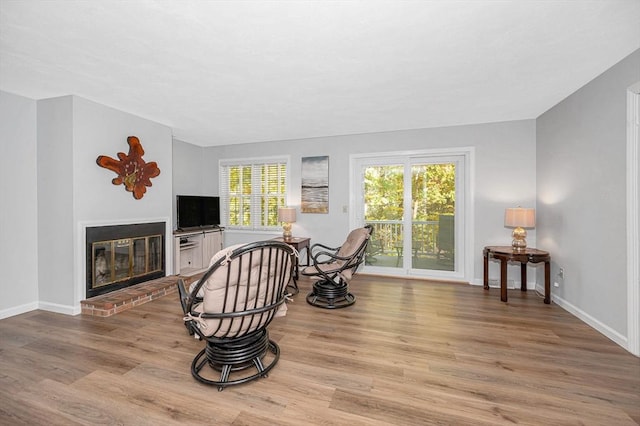 living area featuring a brick fireplace, baseboards, and light wood finished floors