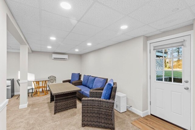 living room with light colored carpet, a drop ceiling, and a wall mounted air conditioner