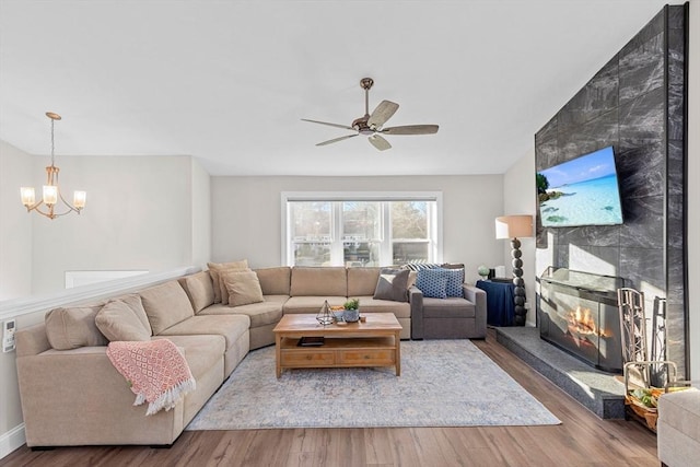 living room featuring ceiling fan with notable chandelier, a fireplace, and hardwood / wood-style flooring