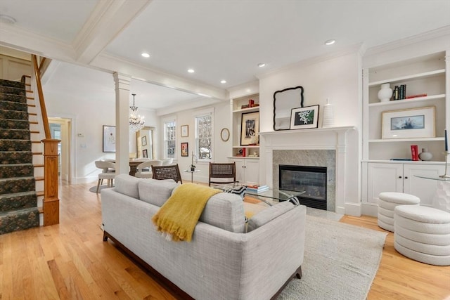 living room with light hardwood / wood-style flooring, built in shelves, beamed ceiling, a fireplace, and ornamental molding