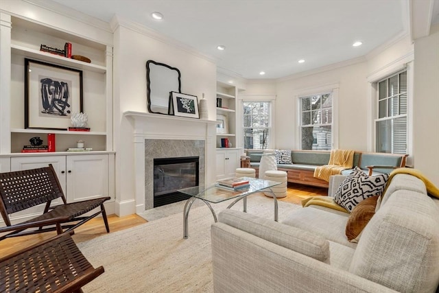 living room with ornamental molding, light hardwood / wood-style flooring, built in shelves, and a premium fireplace