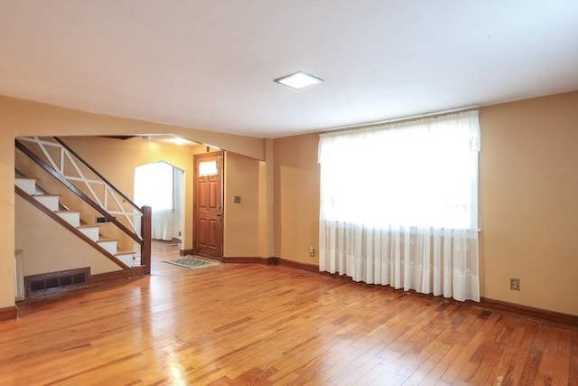 unfurnished living room featuring visible vents, baseboards, stairway, light wood-style floors, and arched walkways