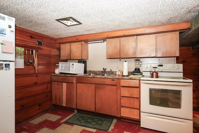 kitchen with a sink, white appliances, brown cabinetry, and dark floors