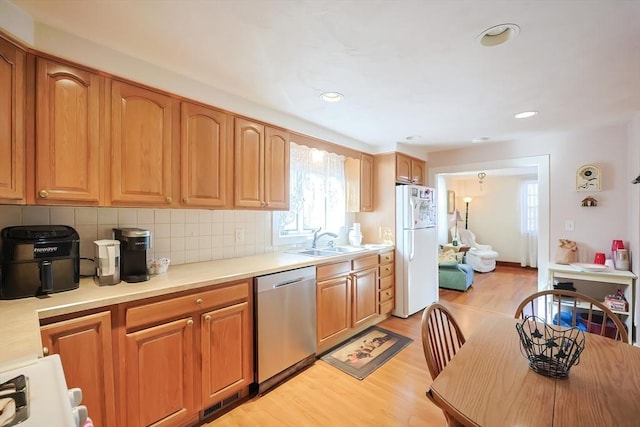 kitchen featuring light wood finished floors, dishwasher, light countertops, freestanding refrigerator, and a sink