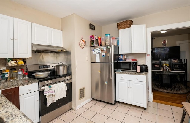 kitchen with dark stone countertops, white cabinetry, light tile patterned flooring, and stainless steel appliances