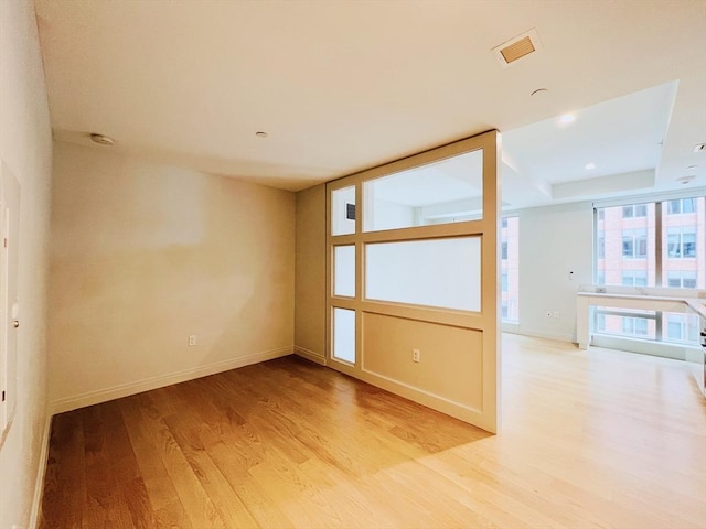 unfurnished room with light hardwood / wood-style flooring and a raised ceiling