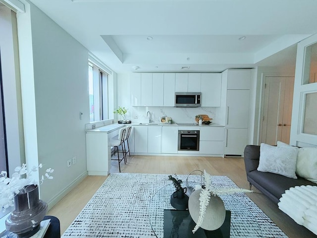 living room featuring light wood-type flooring, a tray ceiling, and sink