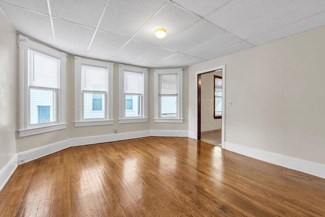 unfurnished room with plenty of natural light, wood-type flooring, and a drop ceiling