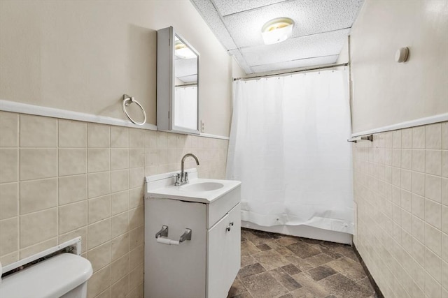 bathroom with tile walls, vanity, a paneled ceiling, and toilet