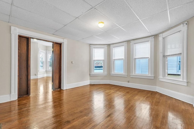 empty room with hardwood / wood-style flooring, a paneled ceiling, and a healthy amount of sunlight