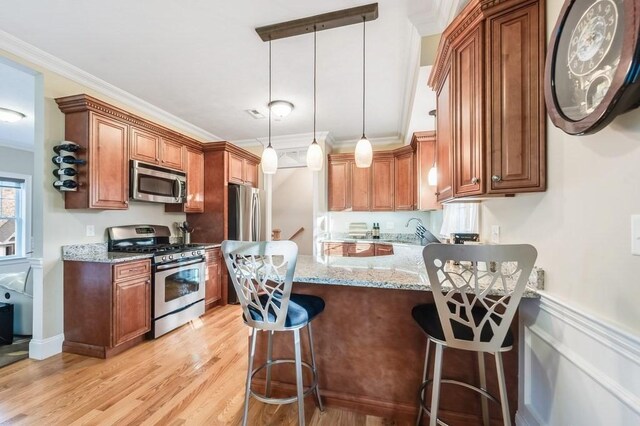 kitchen featuring kitchen peninsula, ornamental molding, stainless steel appliances, pendant lighting, and a breakfast bar area