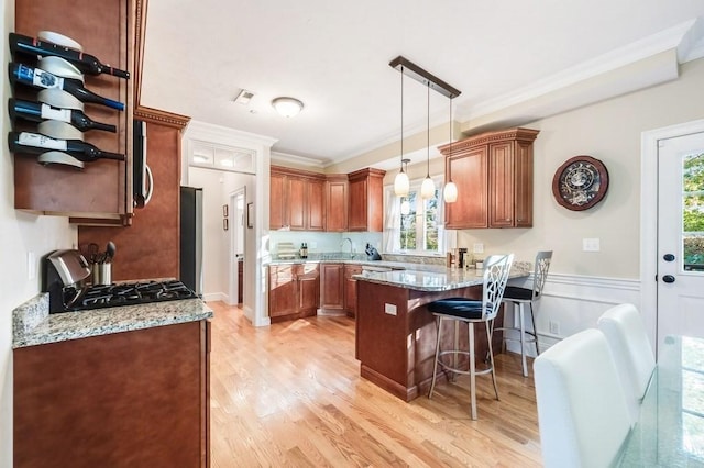 kitchen with a kitchen bar, light stone countertops, light wood-type flooring, crown molding, and range