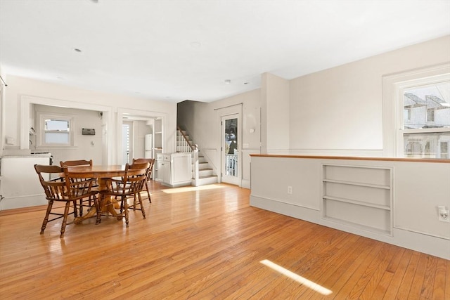 dining area with light wood finished floors, plenty of natural light, stairway, and baseboards