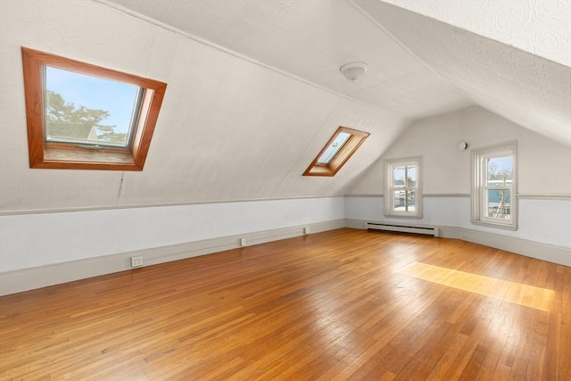 additional living space featuring a textured ceiling, vaulted ceiling with skylight, a baseboard radiator, and hardwood / wood-style flooring