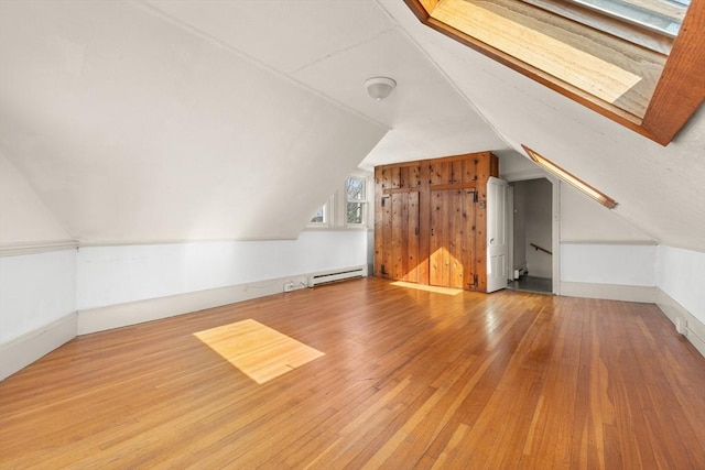 bonus room with a baseboard radiator, wood-type flooring, vaulted ceiling with skylight, and baseboards