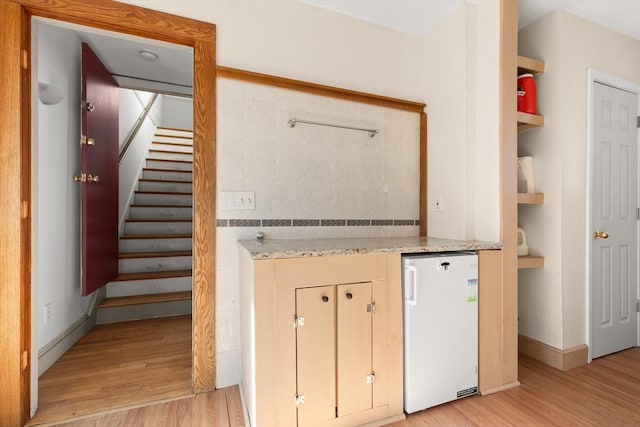 interior space with light stone counters, refrigerator, open shelves, light wood-style flooring, and baseboards