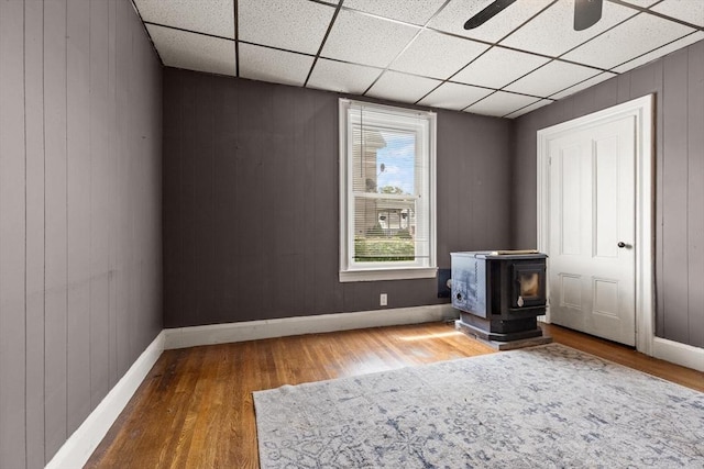 57 Bessom St, Lynn, MA 01902 - unfurnished bedroom with a wood stove, wood finished floors, a paneled ceiling, wooden walls, and ceiling fan