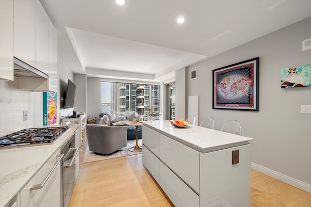 kitchen with white cabinets, light stone counters, light hardwood / wood-style floors, and stainless steel appliances