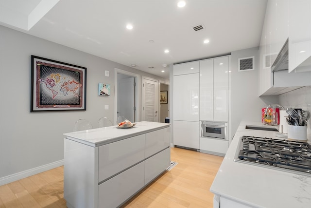 kitchen featuring white cabinets, stainless steel gas cooktop, a kitchen island, light wood-type flooring, and sink